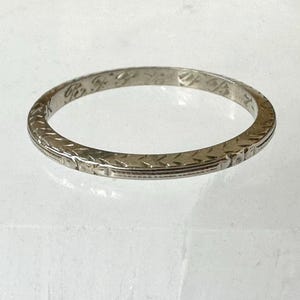 May include: A silver-colored ring with an engraved pattern. The ring has a repeating geometric design around the band. The ring is circular and appears to be made of metal.