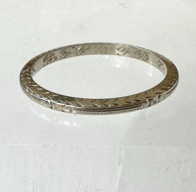May include: A silver-colored ring with an engraved pattern. The ring has a repeating geometric design around the band. The ring is circular and appears to be made of metal.