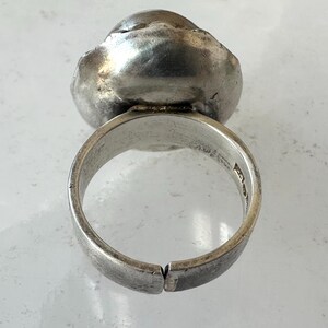 May include: A silver ring featuring a large, textured, rounded stone. The adjustable ring band has markings inside. The stone has a unique, organic shape, and the metal has a slightly tarnished appearance.