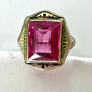 May include: A pink gemstone ring with a gold and green enamel setting. The ring has a square-shaped stone and a decorative design.
