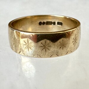 May include: A gold-colored ring with a wide band. The ring's surface is etched with a repeating pattern of starburst designs. The ring has a slightly worn appearance, suggesting age or use.