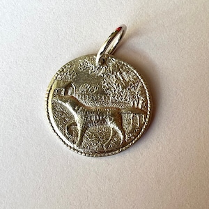 May include: Silver-toned metal dog tag keychain with a detailed image of a dog running. The tag has a ring attached for attaching to keys.