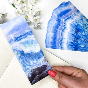 May include: A set of blue and white watercolor bookmarks featuring a crashing wave. The bookmarks are printed on high-quality cardstock and are perfect for adding a touch of whimsy to your reading experience.