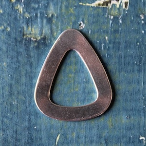 Puede incluir: Un colgante de metal en forma de lágrima con un centro hueco. El colgante tiene un acabado cepillado de color bronce y está sobre una superficie de madera desgastada de color verde azulado. Es un componente de joyería.