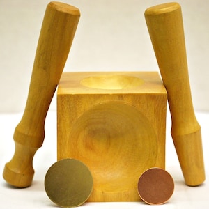 Könnte beinhalten: Ein Werkzeug zur Schmuckherstellung aus Holz mit quadratischer Basis und einer abgerundeten Vertiefung. Zwei Holzhammer sind im Lieferumfang enthalten. Das Werkzeug wird verwendet, um kuppelförmige Schmuckstücke zu erstellen.
