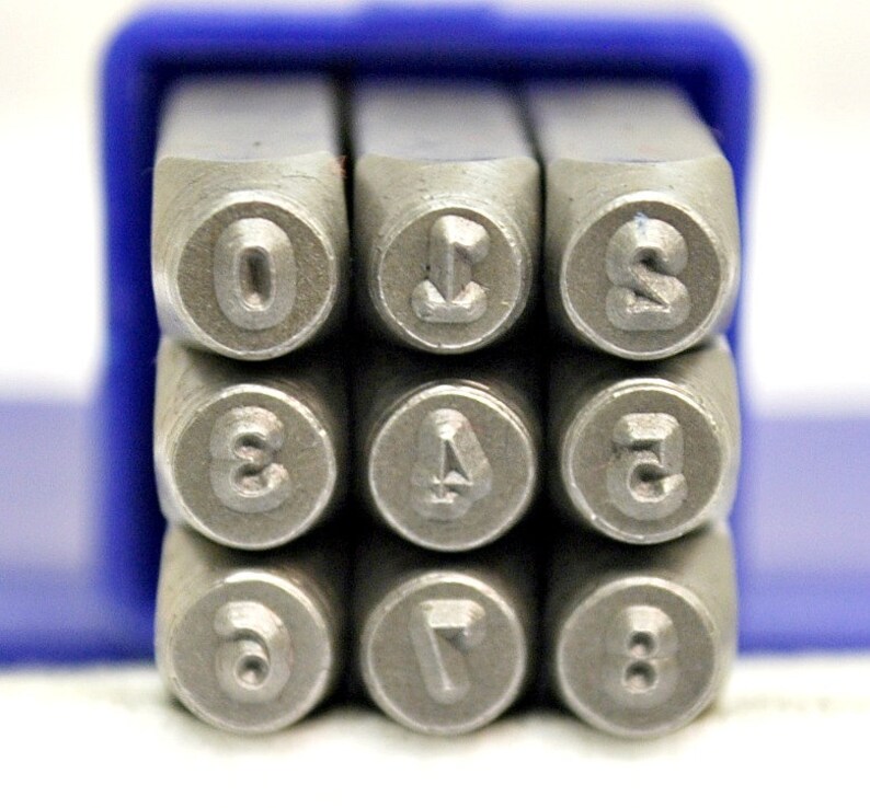 May include: A set of ten metal number stamps in a blue plastic case. The stamps are arranged in two rows of five, with the numbers 0 through 9 visible. The stamps are used for marking metal.