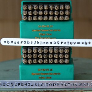 May include: Two sets of metal letter stamps in green plastic cases. The top case contains lowercase letters and the bottom case contains uppercase letters. Each case has 27 stamps, measuring 3 mm each. The cases are labeled "Lowercase Cinnamon Cake Letter Set" and "Uppercase Cinnamon Cake Letter Set".