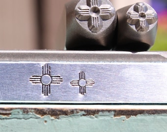May include: Two metal stamps with a design of the Zia symbol, a traditional symbol of the Pueblo people of New Mexico. The stamps are used to create impressions on metal. The Zia symbol is a cross with four circles at the ends of the arms.