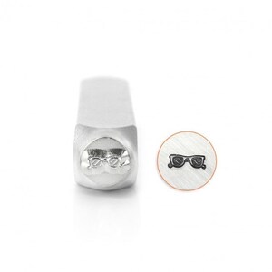 May include: A silver metal stamp with a design of sunglasses. The stamp is used for creating custom jewelry and other crafts.