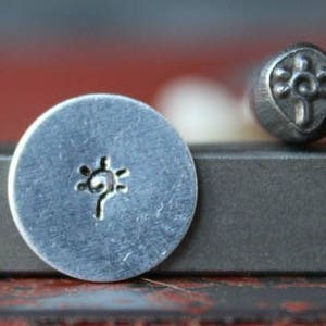 May include: A close-up of two metal stamps, one with a sun design and the other with a flower design. The stamps are on a gray surface.