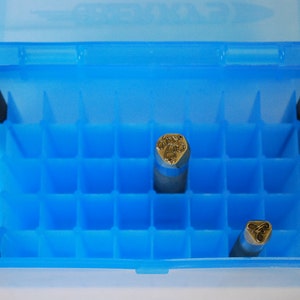 May include: A blue plastic storage case with a grid of compartments. The case contains five metal stamps with different designs.