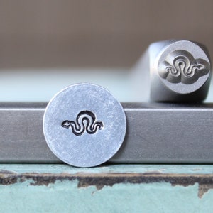 May include: A metal stamp with a snake design. The stamp is used to create impressions in metal.