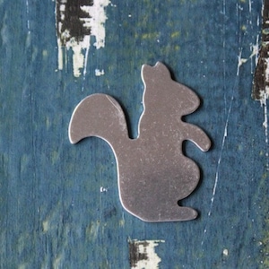 May include: A silver metal squirrel cutout on a blue painted wooden background.