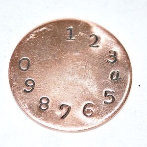 May include: A copper-colored metal disc with the numbers 1 through 9 printed around the edge.