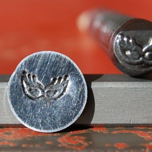 Puede incluir: Un primer plano de un sello de metal con un diseño de dos manos juntas. El sello está sobre una superficie gris y el diseño es visible en el metal.