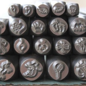 May include: A set of 20 metal stamps with various designs, including hearts, flowers, and abstract patterns. The stamps are arranged in a pyramid shape, with the largest stamp at the top and the smallest stamps at the bottom.