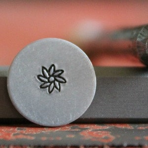 May include: Close-up of a metal stamp with a flower design. The stamp is used to create impressions on metal.