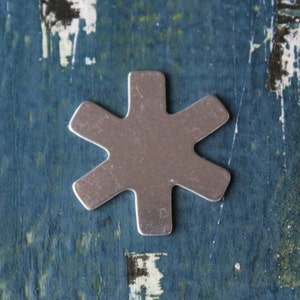 May include: A silver six-pointed star shape, resembling a snowflake, on a blue background.