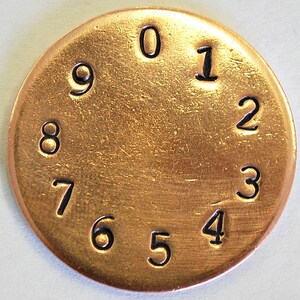 May include: A gold-colored metal disc with the numbers 0 through 9 printed around the edge in black.