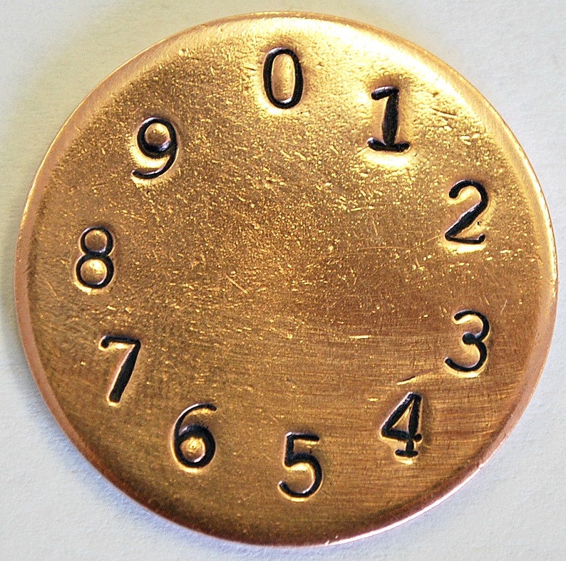 May include: A gold-colored metal disc with the numbers 0 through 9 printed around the edge in black.