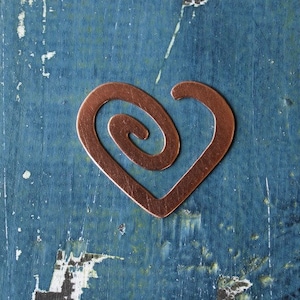 May include: A copper heart-shaped pendant with a spiral design. The pendant is on a blue background.