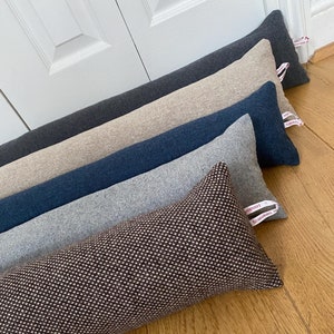 以下が含まれることがあります： グレー、ベージュ、ネイビーブルー、ライトグレー、ブラウンなど、さまざまな色とパターンで構成された6つのドアストッパーのスタック。ドアストッパーはファブリック製で、「EcoDoorStop」というテキストのラベルが付いています。