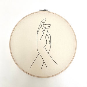 embroidery hoop with drawing of hands holding on white canvas.