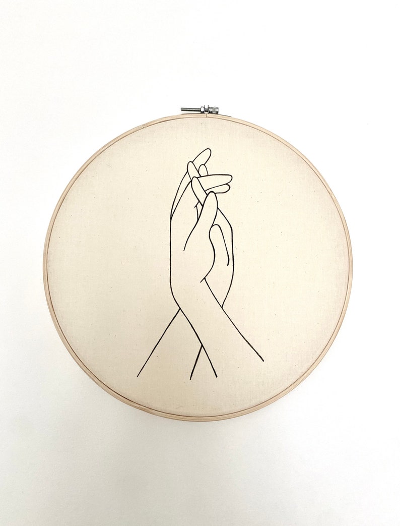 embroidery hoop with drawing of hands holding on white canvas.