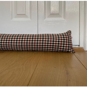 Può includere: Un fermaporta in tessuto a quadri rossi, neri e bianchi. Il fermaporta è di forma cilindrica.