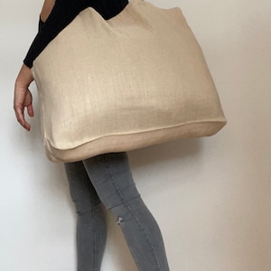 Extra large Natural Jute tote bag worn by woman wearing grey denim trousers and dark top.