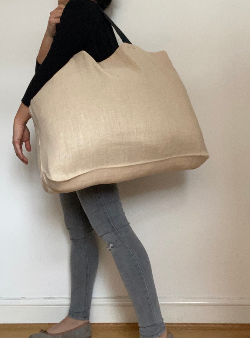 Extra large Natural Jute tote bag worn by woman wearing grey denim trousers and dark top.