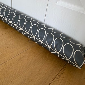 Puede incluir: Un tope de puerta gris con un patrón geométrico blanco. El tope de puerta está hecho de tela y está enrollado.