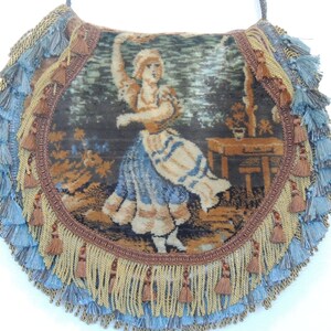 Pode incluir: Uma bolsa vintage de tape&ccedil;aria com franjas azuis e douradas. A bolsa apresenta uma imagem tecida de uma mulher com um vestido azul e branco.