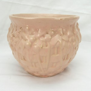Pode incluir: Um vaso de cerâmica rosa claro com um design texturizado e em relevo. O vaso tem uma forma arredondada com uma abertura larga e um padrão detalhado de formas repetidas no exterior. A cor é um rosa suave e discreto.