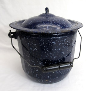 May include: A vintage blue enamelware pot with a lid. The pot has a speckled pattern of white and blue dots. It features a wire handle and a black wooden handle. The lid has a small handle on top. A classic piece of kitchenware.