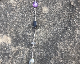 May include: A long silver chain earring with a purple, black, grey, and red gemstone pendant.