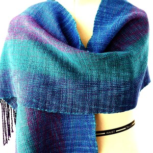 Multi-color handwoven Tencel and Alpaca Scarf. Warp colors include Iris, Amethyst, Red-Violet, Teal Green tencel in broad, blended stripes. Hand-painted soft alpaca in shades of blue and green form the weft. Size is 13.75 inches wide by 70 inches long.Finished with a hand twisted fringe. Hand wash warm, lay flat to dry.
