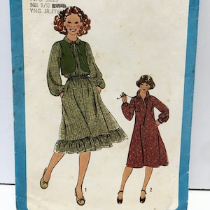 Può includere: Modello di cucito Simplicity numero 8703 per due abiti. Il modello include due taglie, 9/10 e giovane junior/adolescente. Il modello mostra due ragazze che indossano gli abiti. La prima ragazza indossa un abito a quadri verdi e bianchi con un gilet verde. La seconda ragazza indossa un abito rosso con un colletto bianco.