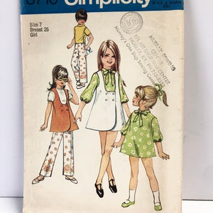 May include: Simplicity sewing pattern number 8716 for girls' dresses and pants. The pattern includes three different styles: a white dress with a green bow, a green floral dress, and pants with a brown vest. The pattern is for sizes 7, with a 26-inch bust.