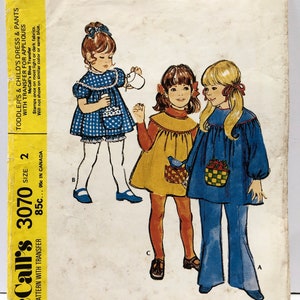 Könnte beinhalten: Vintage McCall's Nähmuster für ein Kleinkind- und Kinderkleid und eine Hose. Das Muster enthält einen blauen Transfer für Applikationen. Die Musternummer ist 3070, Größe 2. Das Muster ist mit einem Transfer bedruckt.