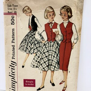 May include: Vintage Simplicity sewing pattern for a sub-teen girl's dress with a vest. The pattern number is 2596 and the price is 50 cents. The pattern shows three different styles of the dress, one with a plaid skirt and two with solid skirts.
