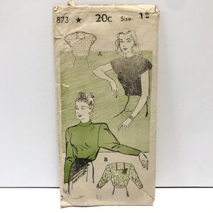 Könnte beinhalten: Vintage-Schnittmuster für eine Bluse mit hohem Kragen und langen Ärmeln. Das Schnittmuster ist auf einem grün-weißen Hintergrund gedruckt und enthält Anleitungen für zwei verschiedene Stile. Die Schnittmuster-Nummer ist 873 und die Größe ist 12.