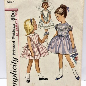 May include: Simplicity sewing pattern number 5338 for a child's dress. The pattern includes three different styles: a white dress with a lace trim, a pink and white striped dress, and a lavender dress with a lace trim. The pattern is for size 4 and is printed in Canada.
