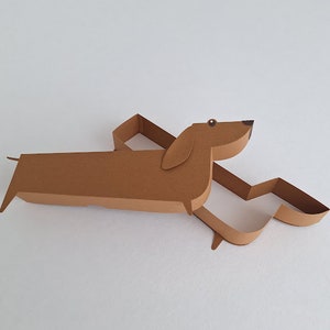 May include: A brown paper dachshund shaped box with a cut-out design. The box is open and the inside is white.