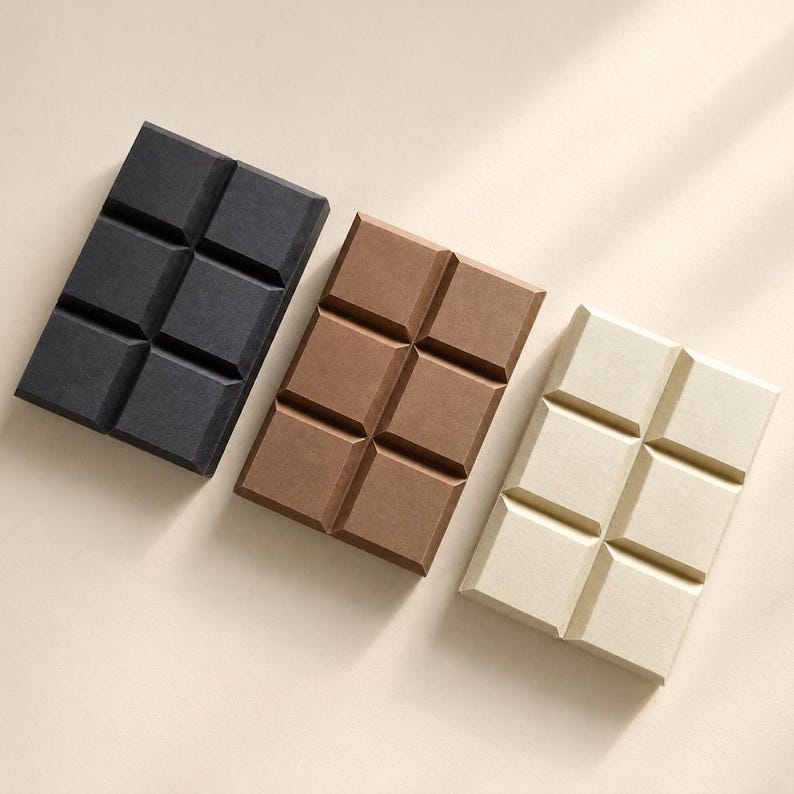 May include: Three rectangular wax melt bars arranged diagonally, each featuring six square segments. The bars are colored in solid black, medium brown, and off-white, with a matte finish and distinct grid lines separating each individual square section.