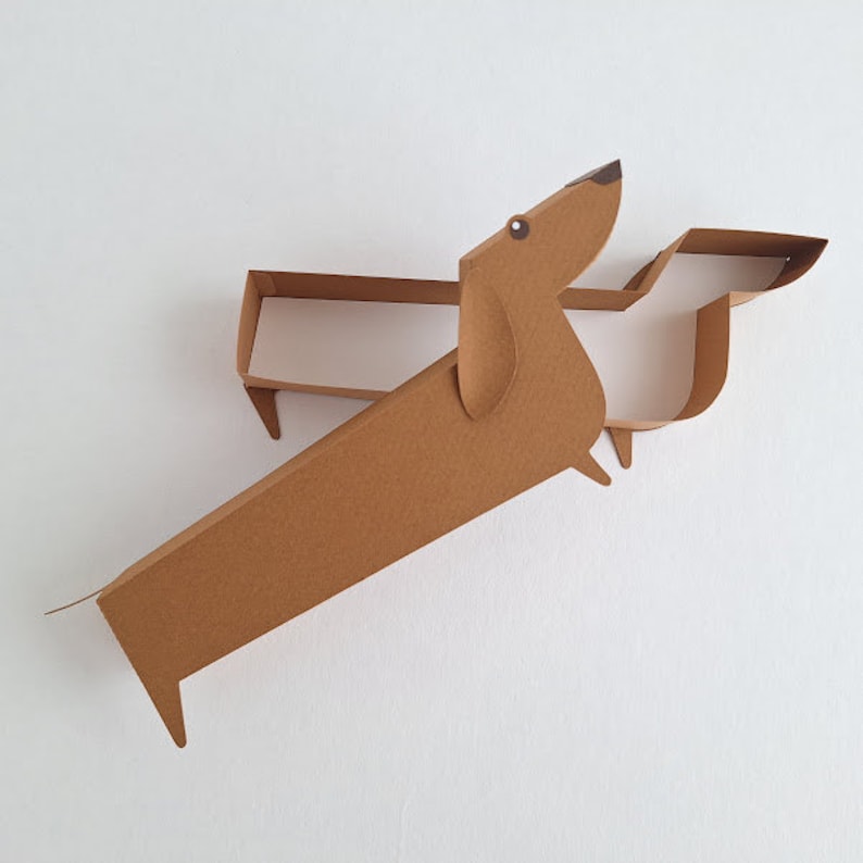 May include: A brown cardboard dachshund cutout with a simple design. The dachshund is standing on its hind legs with its front legs extended forward. The dachshund is made of two pieces of cardboard that are joined together.