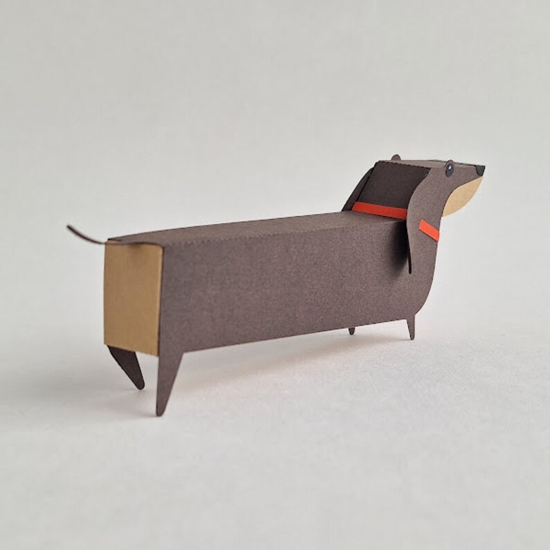 May include: A brown paper dachshund with a red collar. The dachshund is made of paper and has a long, thin body. It is a simple, minimalist design.