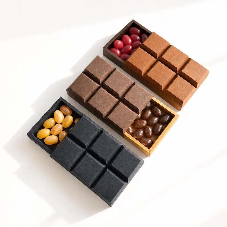May include: Three rectangular sliding boxes shaped like chocolate bars, each with a textured surface. The top box is brown with red candies, the middle box is dark brown with dark candies, and the bottom box is black with yellow candies.