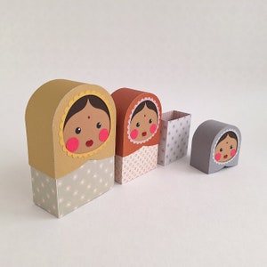 Puede incluir: Conjunto de cuatro cajas encajables con papel estampado de colores y caras de mujeres con mejillas rosadas y cabello negro. Las cajas son de diferentes tamaños y están hechas de cartón.
