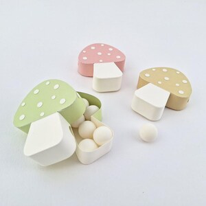 Pode incluir: Tr&ecirc;s caixas em forma de cogumelo, uma verde, uma rosa e uma marrom, com bolinhas brancas. A caixa verde est&aacute; aberta e cheia de doces brancos.